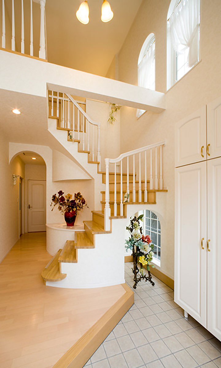 吹き抜けの広い玄関。正面にはアールの形の飾り棚、階段は優美な曲線のサーキュラー階段を採用